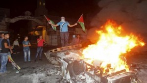 A Palestinian holding Palestinian flags stands on a burning car belonging to Jewish settlers after it was set on fire by Palestinians in the West Bank city of Nablus October 18, 2015. REUTERS/Abed Omar Qusini