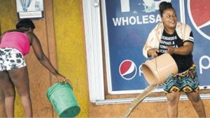 A woman bails out water from her businessplace in the vicinity of the Portia Simpson Miller Square following heavy rain yesterday afternoon.